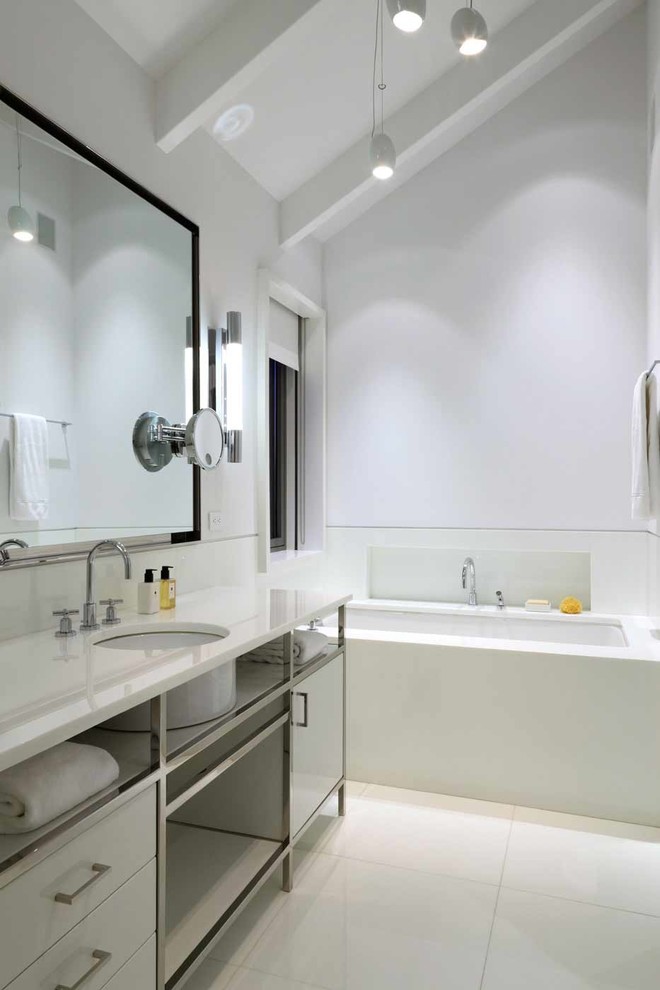 Photo of a contemporary bathroom in New York with a submerged sink, flat-panel cabinets, white cabinets, a submerged bath and white walls.