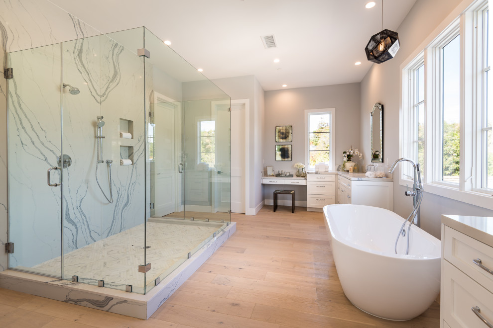 Inredning av ett klassiskt grå grått badrum, med luckor med infälld panel, vita skåp, ett fristående badkar, vit kakel, stenhäll, grå väggar, ljust trägolv och beiget golv