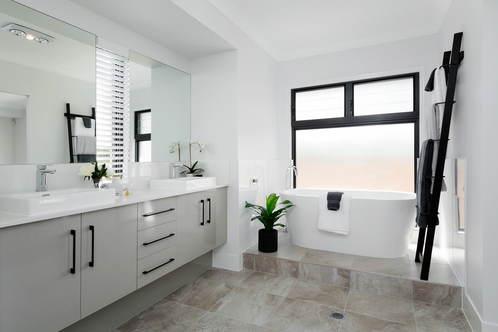 Modernes Badezimmer mit flächenbündigen Schrankfronten, grauen Schränken, freistehender Badewanne, weißen Fliesen, weißer Wandfarbe, Aufsatzwaschbecken und grauem Boden in Brisbane
