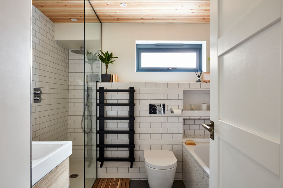 Foto på ett litet badrum med dusch, med ett platsbyggt badkar, en hörndusch, en toalettstol med hel cisternkåpa, vit kakel, keramikplattor, ett avlångt handfat, grått golv och med dusch som är öppen