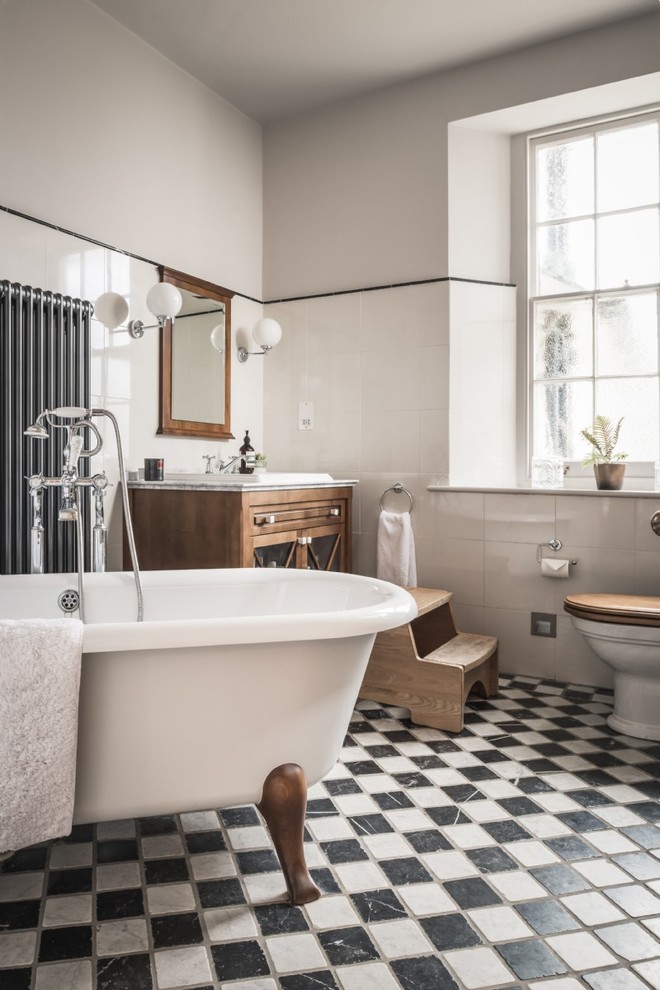 На фото: главная ванная комната в классическом стиле с стеклянными фасадами, фасадами цвета дерева среднего тона, ванной на ножках, белой плиткой, серыми стенами, накладной раковиной и разноцветным полом с