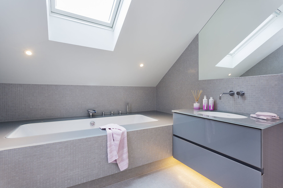 ロンドンにあるコンテンポラリースタイルのおしゃれな浴室 (フラットパネル扉のキャビネット、グレーのキャビネット、グレーのタイル、グレーの壁、アンダーカウンター洗面器、アンダーマウント型浴槽) の写真