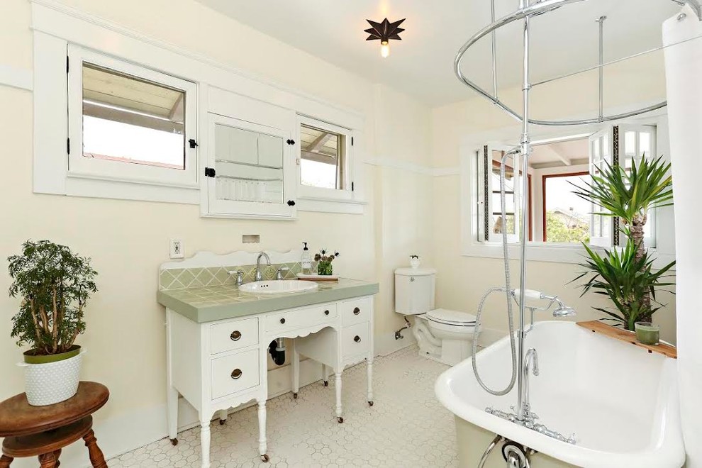 Bild på ett mellanstort amerikanskt grön grönt en-suite badrum, med möbel-liknande, vita skåp, ett badkar med tassar, en dusch/badkar-kombination, en toalettstol med separat cisternkåpa, gula väggar, ett nedsänkt handfat, kaklad bänkskiva, vitt golv och dusch med duschdraperi