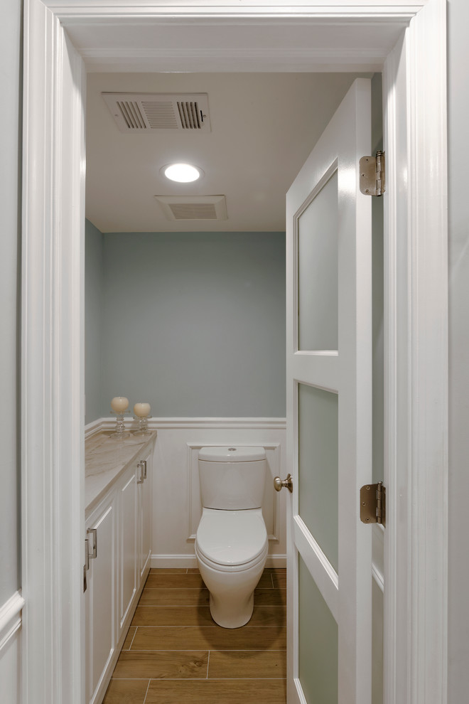 Cette image montre un grand WC et toilettes minimaliste avec un placard avec porte à panneau surélevé, des portes de placard blanches, WC séparés, un mur bleu, un sol en carrelage de terre cuite, un plan de toilette en marbre et un lavabo encastré.