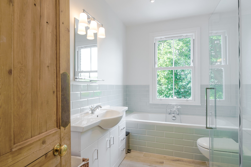 Transitional 3/4 white tile and subway tile beige floor drop-in bathtub photo in Surrey with flat-panel cabinets, white cabinets, a wall-mount toilet, white walls and a console sink