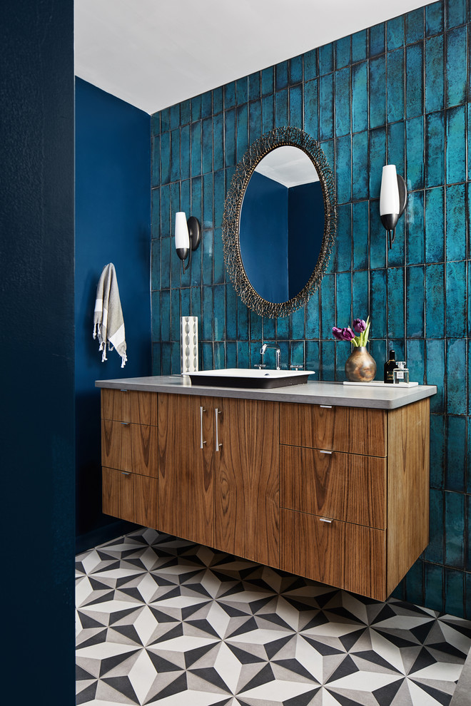 Bild på ett mellanstort funkis grå grått badrum, med blå kakel, släta luckor, skåp i mellenmörkt trä, blå väggar, cementgolv, ett nedsänkt handfat och flerfärgat golv
