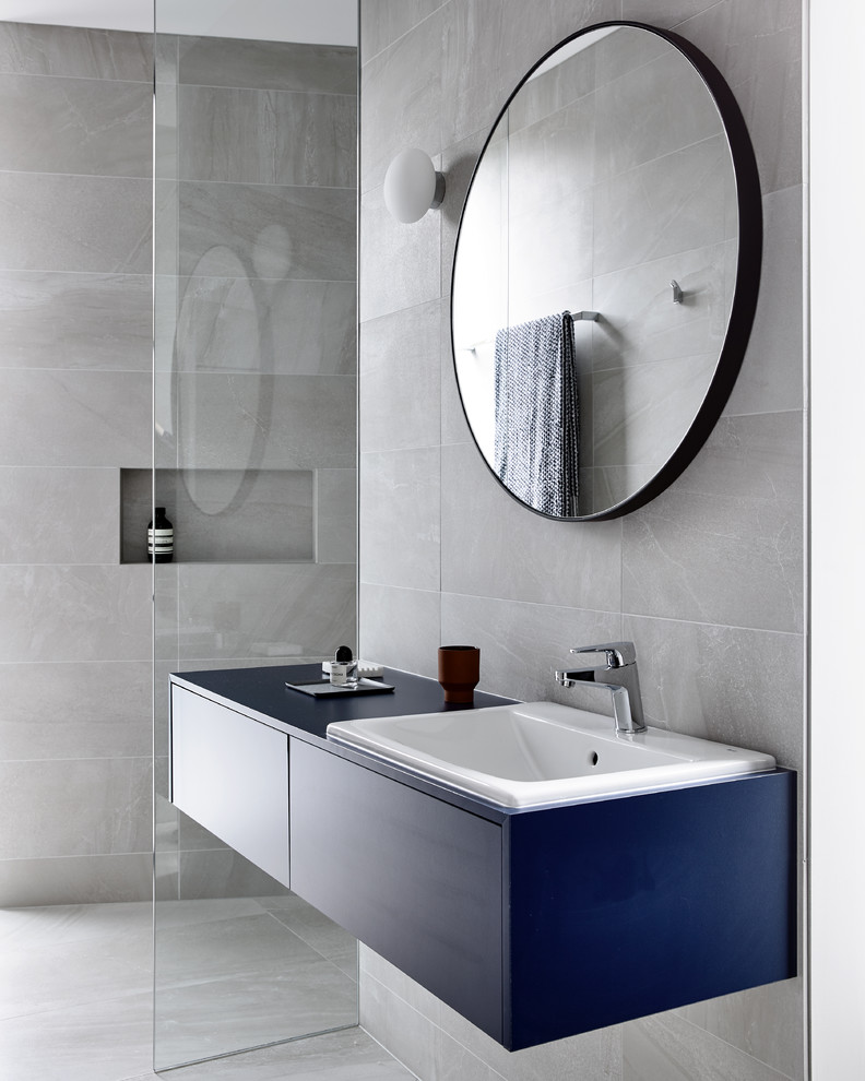 Idéer för att renovera ett stort funkis blå blått badrum, med släta luckor, blå skåp, en dusch i en alkov, en vägghängd toalettstol, grå kakel, keramikplattor, grå väggar, klinkergolv i keramik, ett nedsänkt handfat, laminatbänkskiva, grått golv och med dusch som är öppen