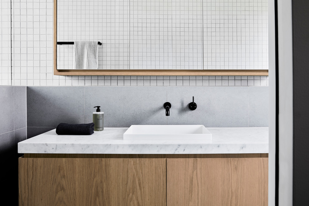 Photo of a small contemporary ensuite bathroom in Melbourne with freestanding cabinets, light wood cabinets, a walk-in shower, a wall mounted toilet, grey tiles, ceramic tiles, white walls, ceramic flooring, a built-in sink, marble worktops, grey floors, an open shower and white worktops.