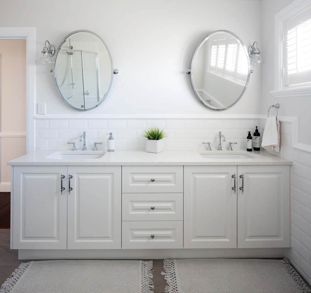 Klassisk inredning av ett stort vit vitt en-suite badrum, med vita skåp, vit kakel, keramikplattor, vita väggar, ett undermonterad handfat, bänkskiva i kvarts, luckor med upphöjd panel och grått golv
