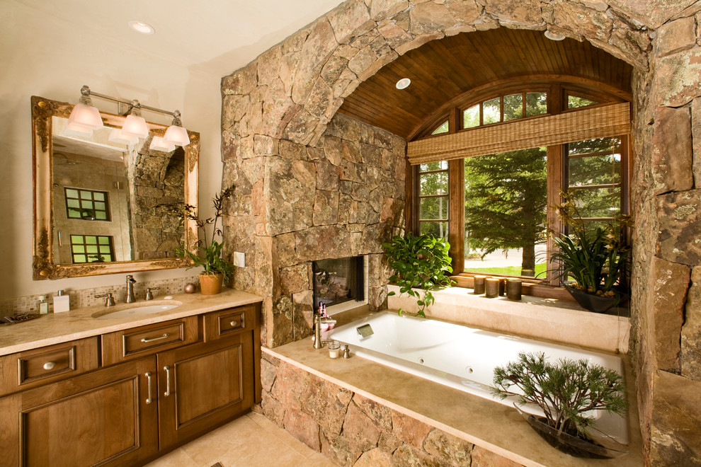 Стильный дизайн: ванная комната в классическом стиле с врезной раковиной, фасадами с утопленной филенкой, фасадами цвета дерева среднего тона, накладной ванной и каменной плиткой - последний тренд