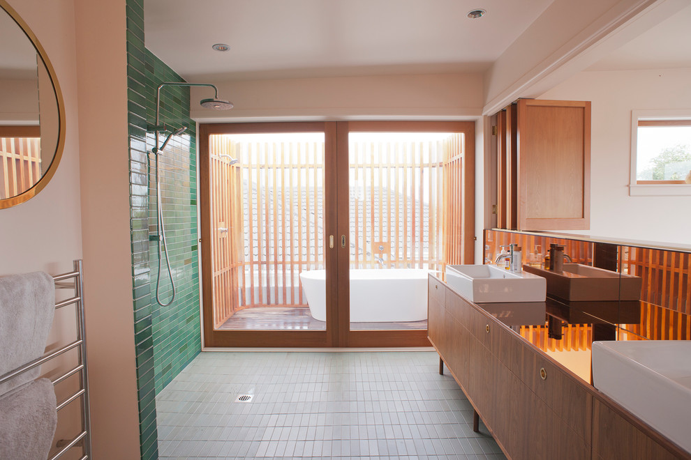 Inspiration pour une grande salle de bain principale minimaliste en bois brun avec un placard à porte plane, un plan de toilette en verre, un carrelage vert, une grande vasque, sol en béton ciré, une baignoire indépendante et une douche ouverte.