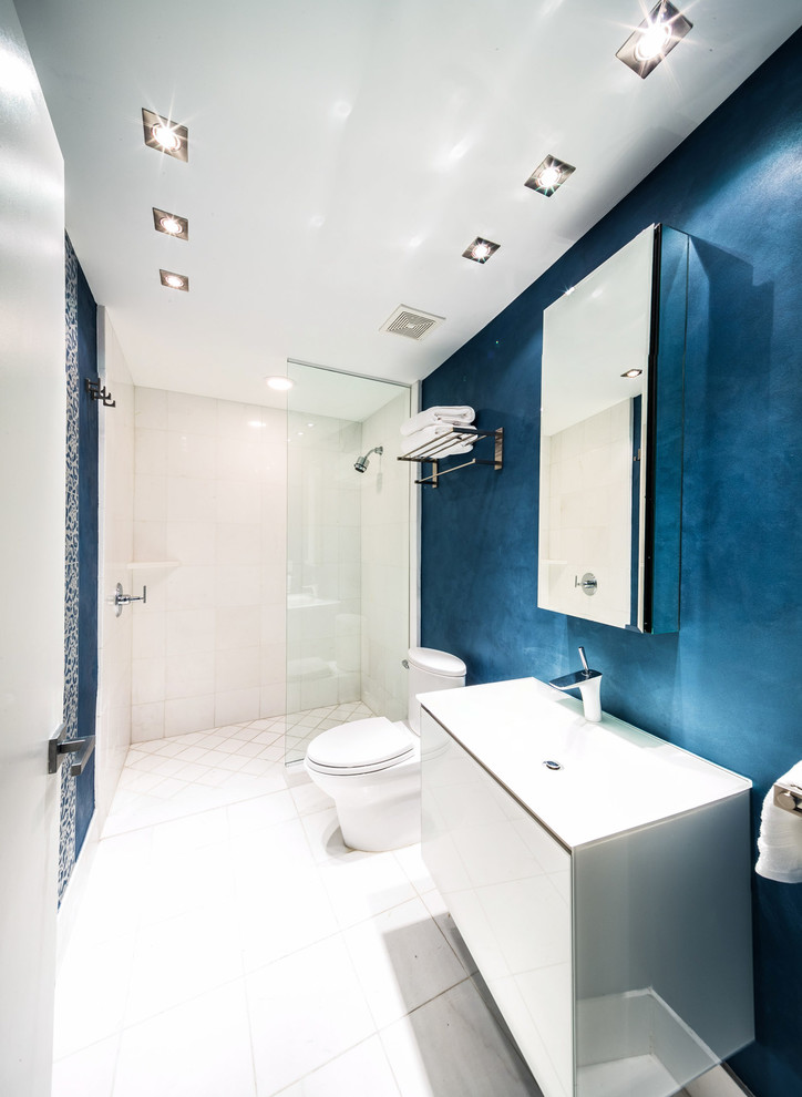 Photo of a modern shower room bathroom in Miami with white cabinets, a walk-in shower, a one-piece toilet, white tiles, blue walls and a built-in sink.