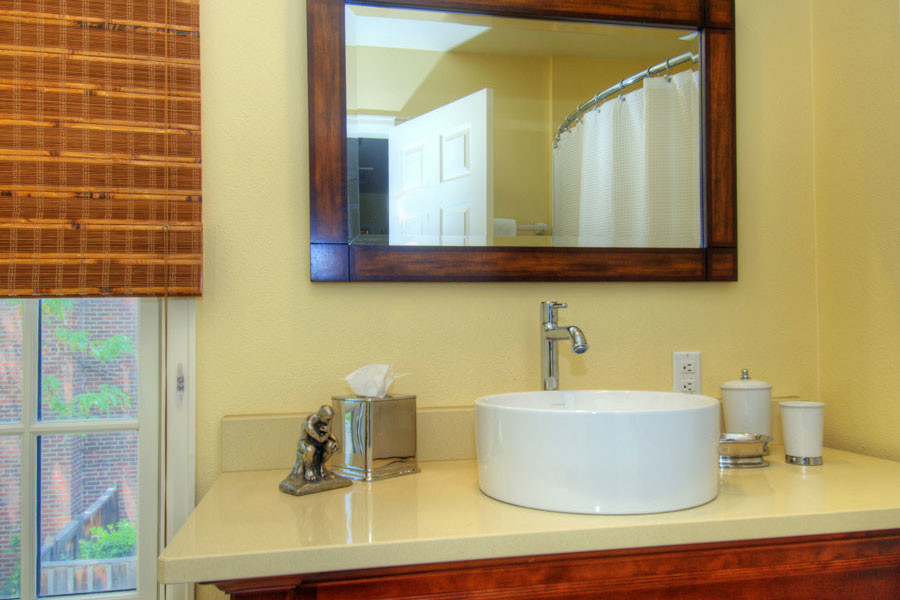 Klassisk inredning av ett mellanstort badrum med dusch, med ett fristående handfat, skåp i mellenmörkt trä och gula väggar