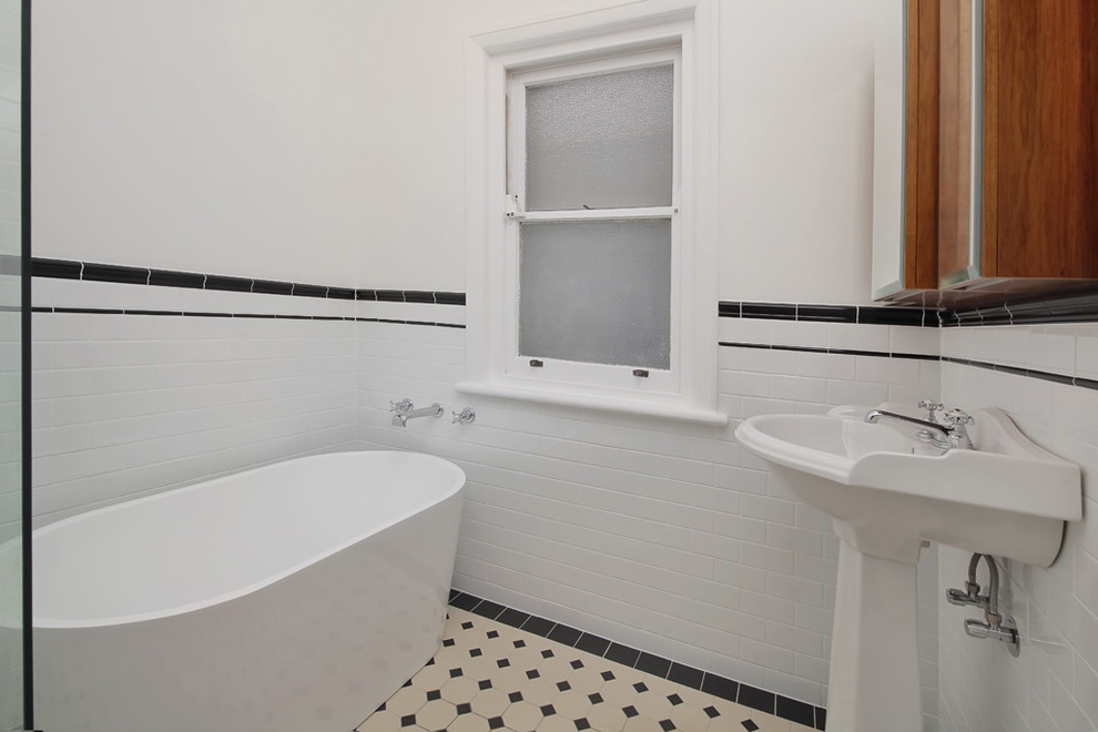 Idéer för små amerikanska vitt badrum med dusch, med luckor med glaspanel, bruna skåp, ett fristående badkar, en hörndusch, en toalettstol med separat cisternkåpa, vit kakel, cementkakel, vita väggar, cementgolv, ett piedestal handfat, träbänkskiva, svart golv och dusch med gångjärnsdörr