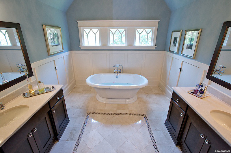 Exemple d'une grande salle de bain principale craftsman en bois foncé avec un lavabo encastré, un placard à porte shaker, un plan de toilette en marbre, une baignoire indépendante, un carrelage beige, un mur bleu, un sol en marbre et un carrelage de pierre.
