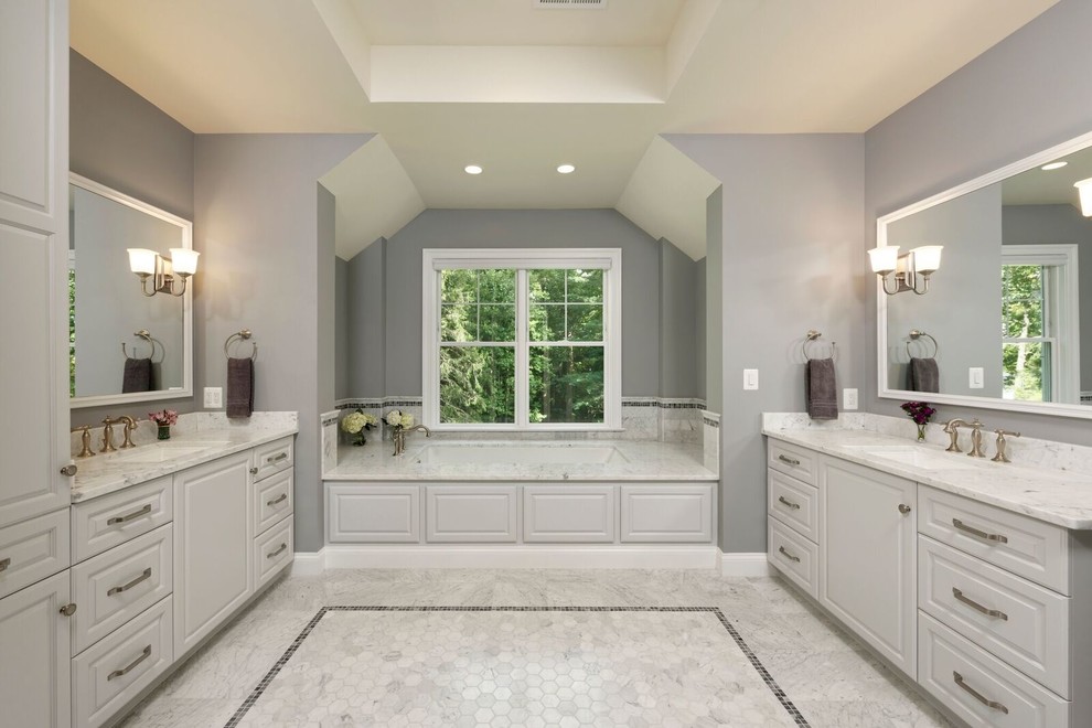 На фото: большая главная ванная комната в современном стиле с фасадами с выступающей филенкой, белыми фасадами, полновстраиваемой ванной, серыми стенами, мраморным полом, врезной раковиной, столешницей из гранита и серым полом