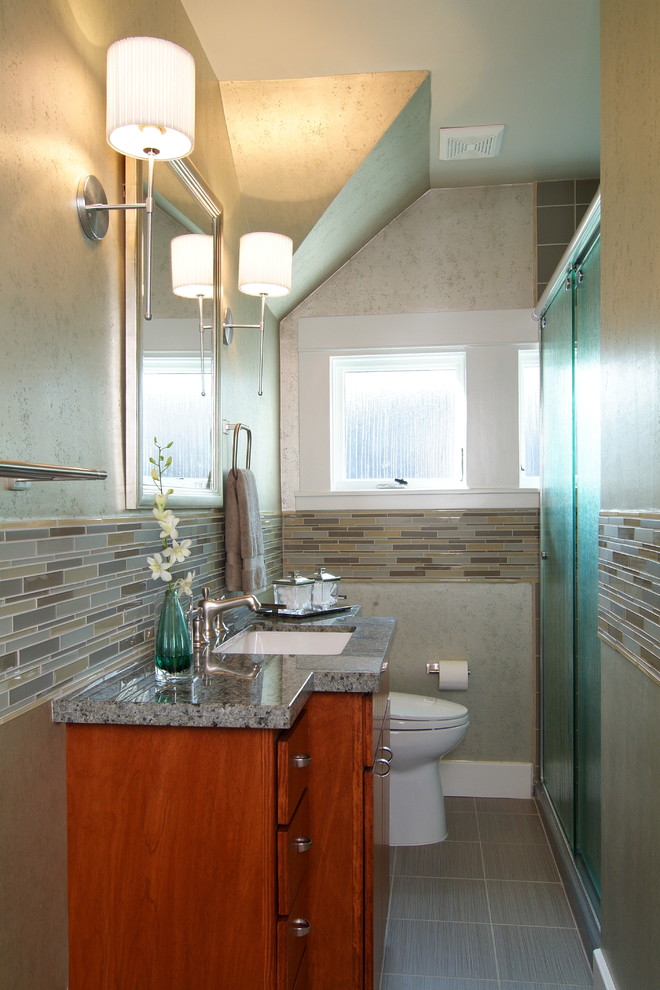 Photo of a small classic ensuite bathroom in Houston with a submerged sink, flat-panel cabinets, medium wood cabinets, granite worktops, an alcove shower, a two-piece toilet, grey tiles, porcelain tiles, grey walls and porcelain flooring.