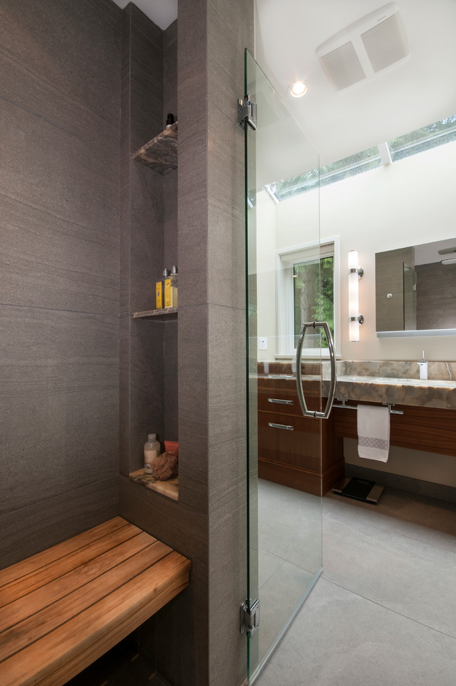 Inredning av ett klassiskt stort en-suite badrum, med ett avlångt handfat, släta luckor, skåp i mellenmörkt trä, bänkskiva i onyx, en kantlös dusch, en vägghängd toalettstol, grå kakel, stenkakel, vita väggar, betonggolv, grått golv och dusch med gångjärnsdörr