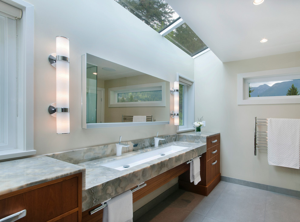 Inredning av ett klassiskt stort en-suite badrum, med ett avlångt handfat, släta luckor, skåp i mellenmörkt trä, bänkskiva i onyx, en kantlös dusch, en vägghängd toalettstol, grå kakel, stenkakel, vita väggar, grått golv och klinkergolv i porslin