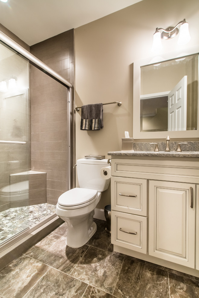 Bild på ett mellanstort vintage badrum med dusch, med luckor med upphöjd panel, vita skåp, en dusch i en alkov, en toalettstol med separat cisternkåpa, grå kakel, porslinskakel, beige väggar, klinkergolv i porslin, ett undermonterad handfat, granitbänkskiva, grått golv och dusch med skjutdörr