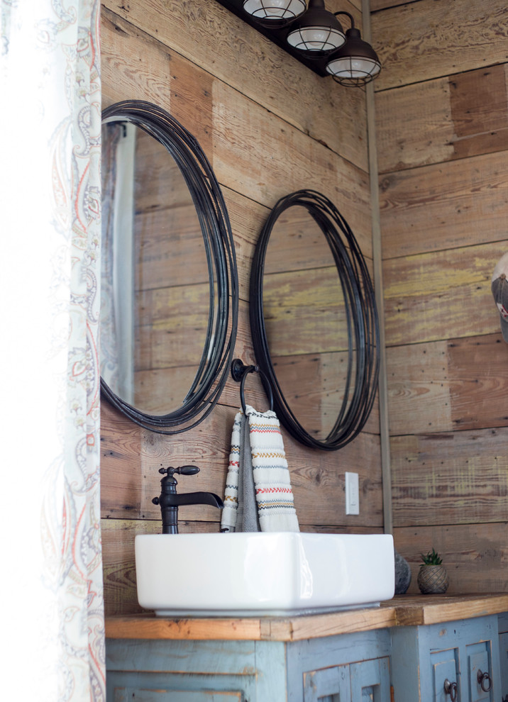 Réalisation d'une salle d'eau champêtre en bois vieilli de taille moyenne avec un placard avec porte à panneau surélevé, une vasque, un plan de toilette en bois, une cabine de douche avec un rideau et un plan de toilette marron.