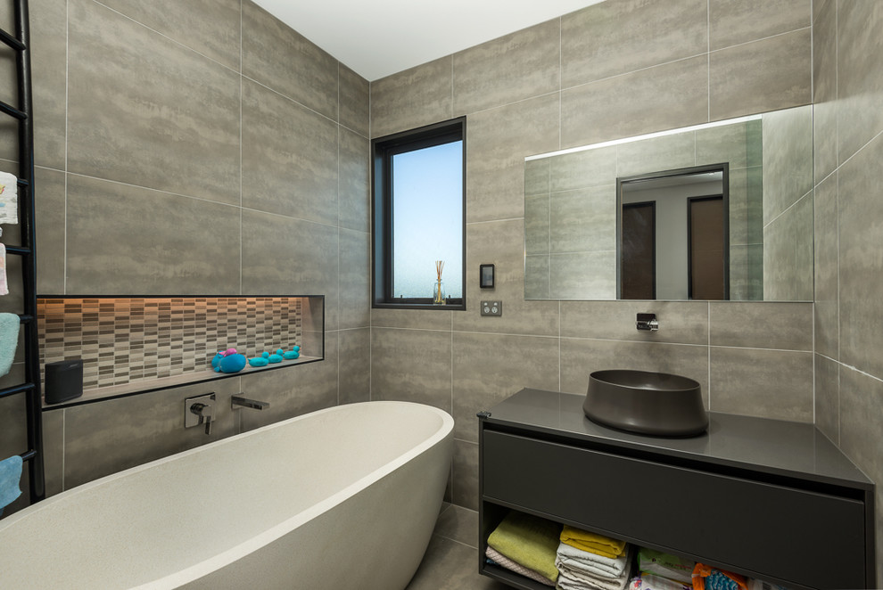 Inspiration pour une salle de bain design avec un placard à porte plane, des portes de placard grises, une baignoire indépendante, une vasque, un sol gris et un plan de toilette gris.