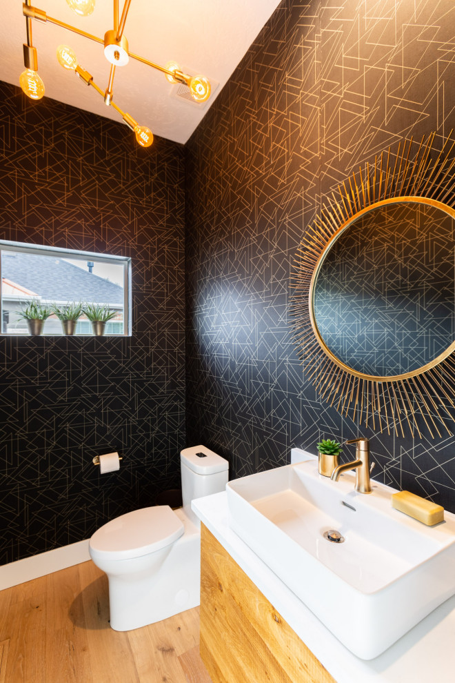 Cette photo montre un WC et toilettes moderne en bois brun avec un placard à porte plane, un mur noir, parquet clair, une vasque, un plan de toilette en quartz modifié et un plan de toilette blanc.