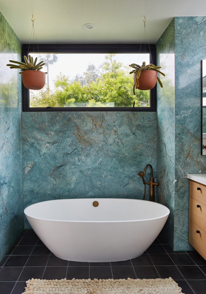 Inspiration for a medium sized retro ensuite bathroom in Los Angeles with flat-panel cabinets, light wood cabinets, a freestanding bath, a corner shower, a one-piece toilet, blue tiles, marble tiles, blue walls, cement flooring, a submerged sink, engineered stone worktops, black floors, a hinged door and white worktops.
