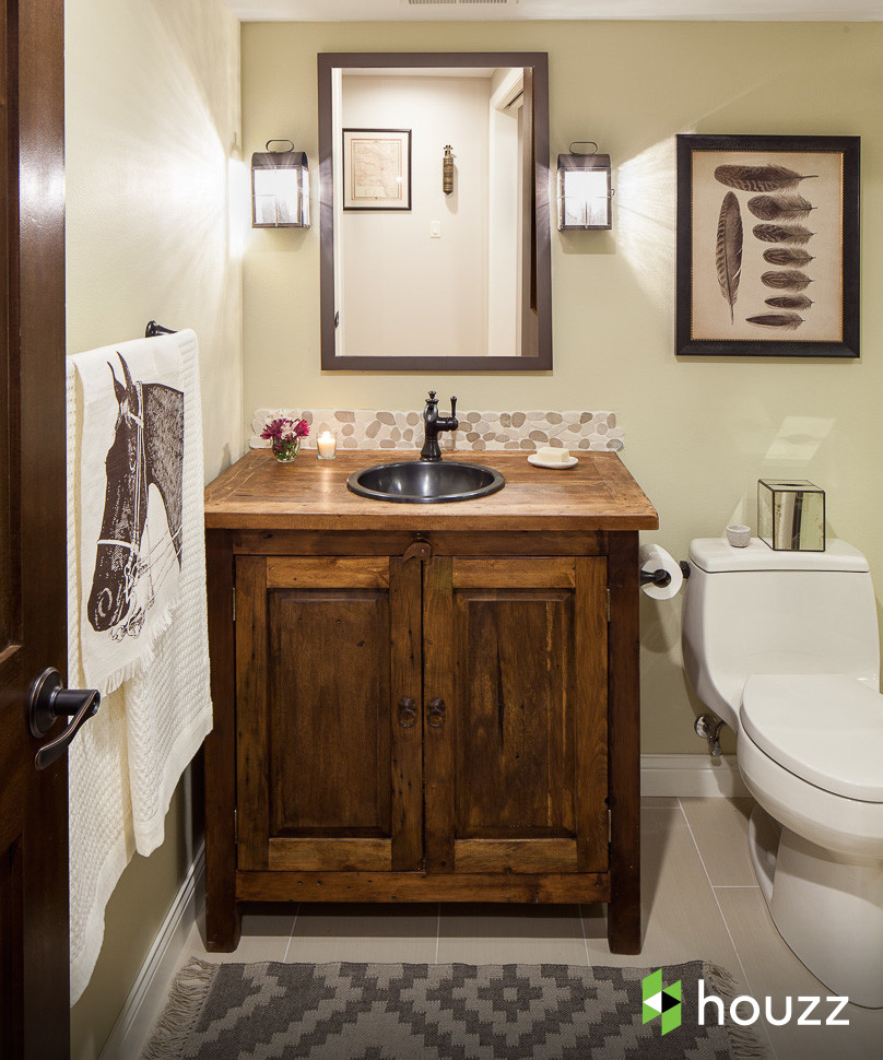 Cette image montre une salle de bain chalet en bois foncé avec un lavabo posé, un placard avec porte à panneau surélevé, WC à poser, un carrelage beige, une plaque de galets et un mur beige.