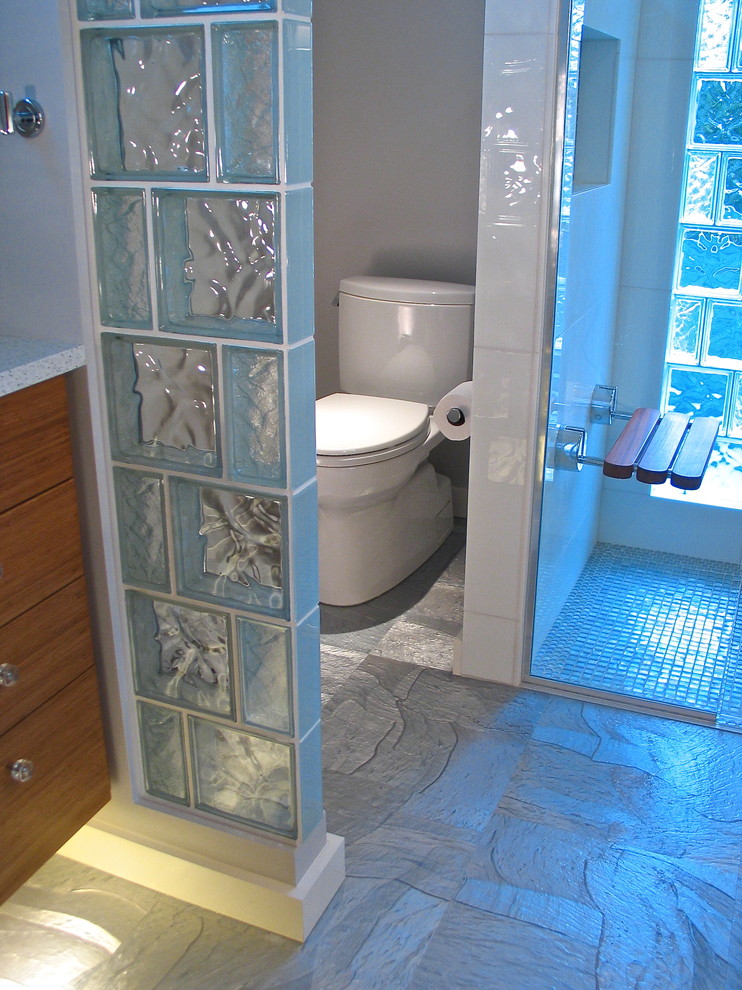 Inredning av ett modernt litet en-suite badrum, med ett undermonterad handfat, släta luckor, skåp i mellenmörkt trä, bänkskiva i kvarts, en kantlös dusch, en toalettstol med separat cisternkåpa, vit kakel, glaskakel, grå väggar och linoleumgolv