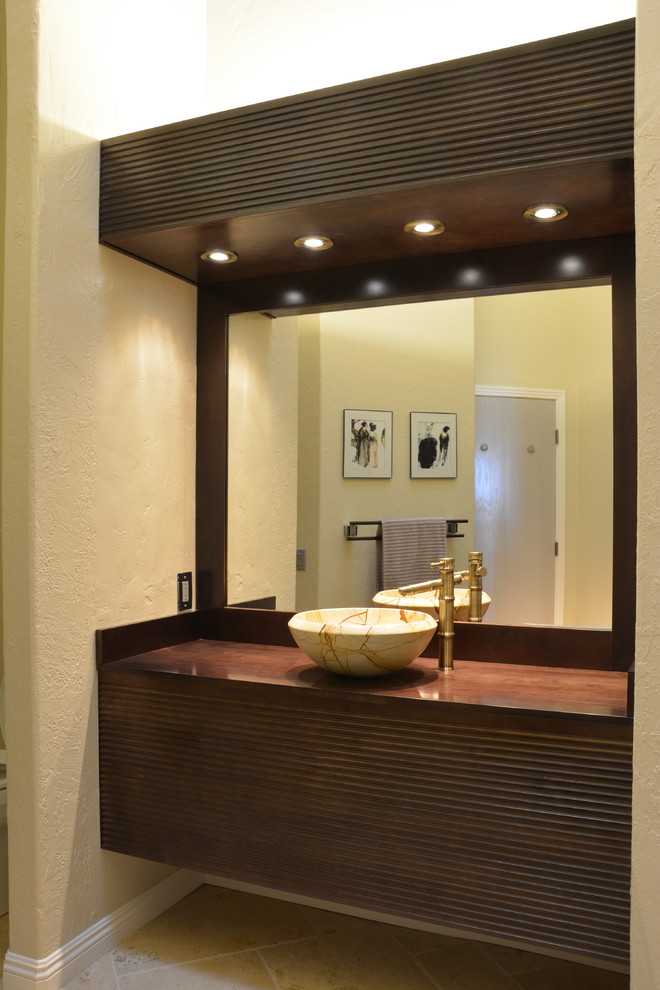 Пример оригинального дизайна: ванная комната среднего размера в восточном стиле с фасадами островного типа, темными деревянными фасадами, бежевой плиткой, каменной плиткой, желтыми стенами, полом из травертина, душевой кабиной, настольной раковиной и столешницей из дерева