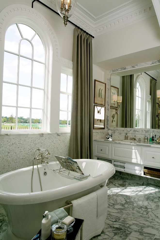 Photo of a large classic ensuite bathroom in Houston with a built-in sink, raised-panel cabinets, white cabinets, marble worktops, a freestanding bath, a one-piece toilet, grey tiles, mosaic tiles, beige walls and marble flooring.