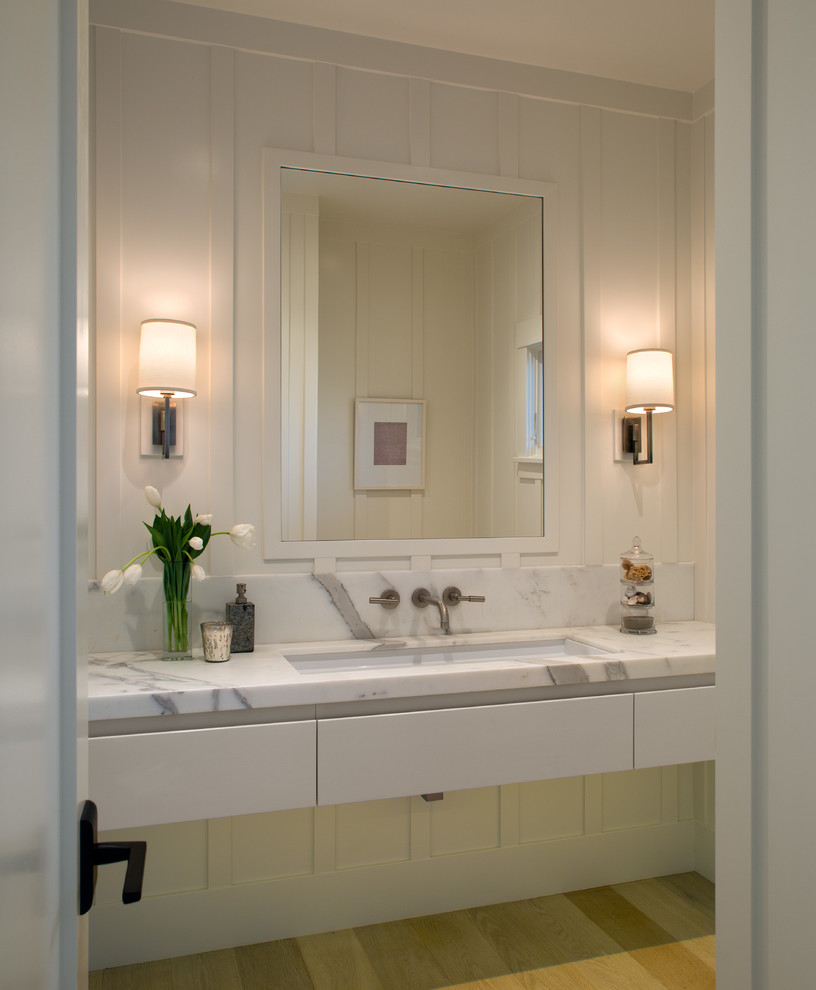 Cette photo montre une salle d'eau chic de taille moyenne avec un lavabo encastré, un placard à porte plane, des portes de placard blanches, un plan de toilette en marbre, un mur blanc et parquet clair.