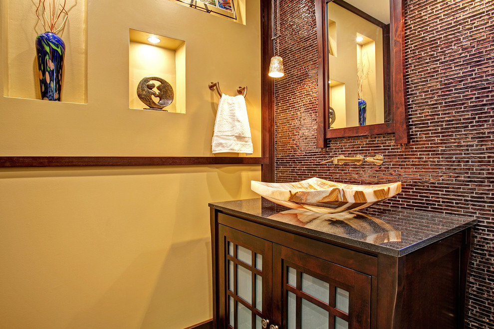 Asiatisk inredning av ett mellanstort badrum med dusch, med ett fristående handfat, luckor med glaspanel, skåp i mörkt trä, granitbänkskiva, en toalettstol med separat cisternkåpa, brun kakel, mosaik och gula väggar
