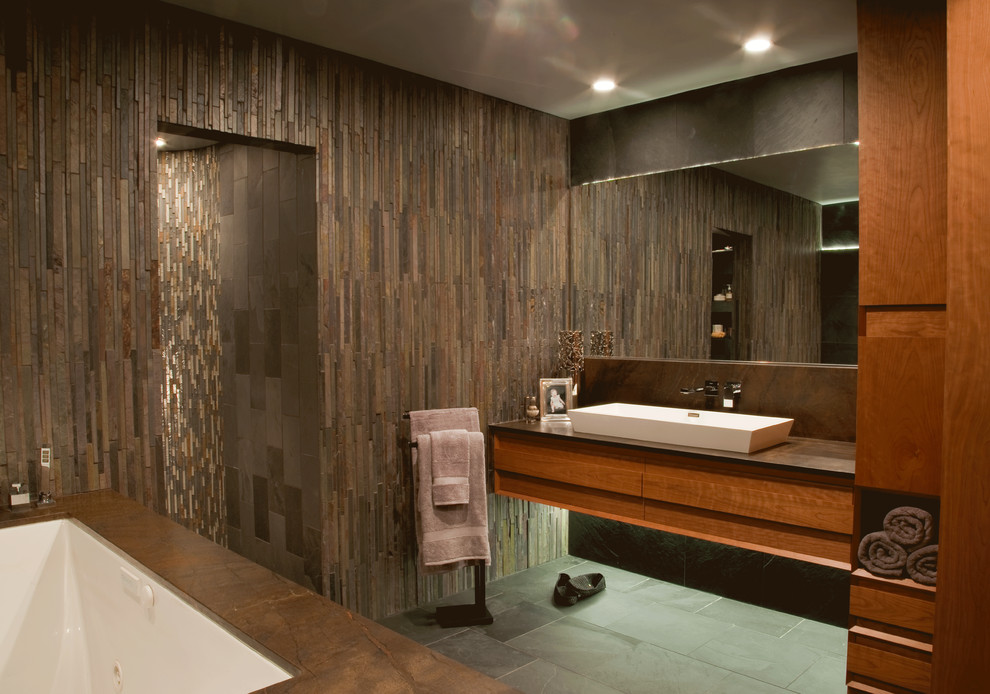 Example of a large trendy master slate floor doorless shower design in San Diego with a trough sink, furniture-like cabinets, medium tone wood cabinets, limestone countertops, an undermount tub and brown walls