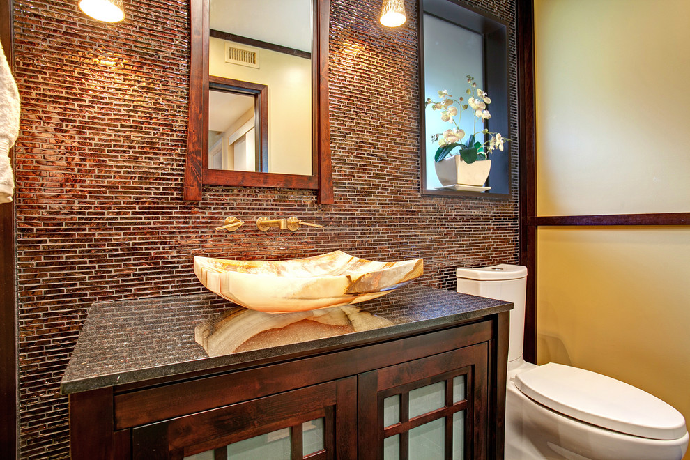 Mid-sized asian 3/4 brown tile and mosaic tile bathroom photo in San Diego with a vessel sink, glass-front cabinets, dark wood cabinets, granite countertops, a two-piece toilet and yellow walls