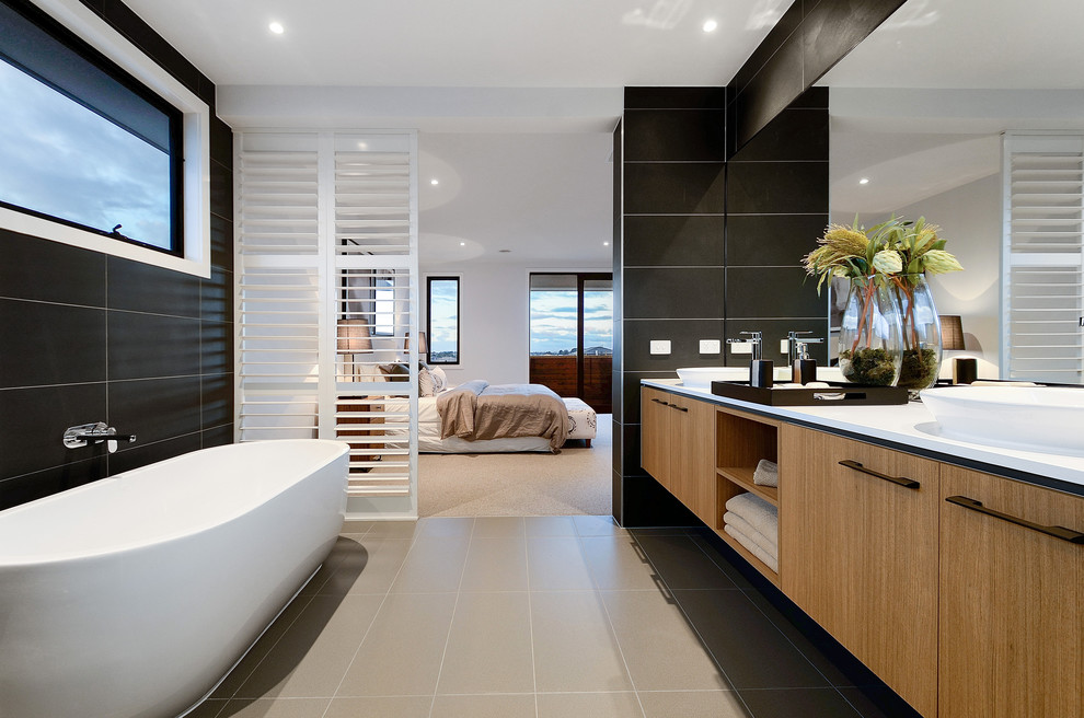 Inredning av ett modernt en-suite badrum, med släta luckor, skåp i ljust trä, ett fristående badkar, svart kakel, svarta väggar och ett fristående handfat