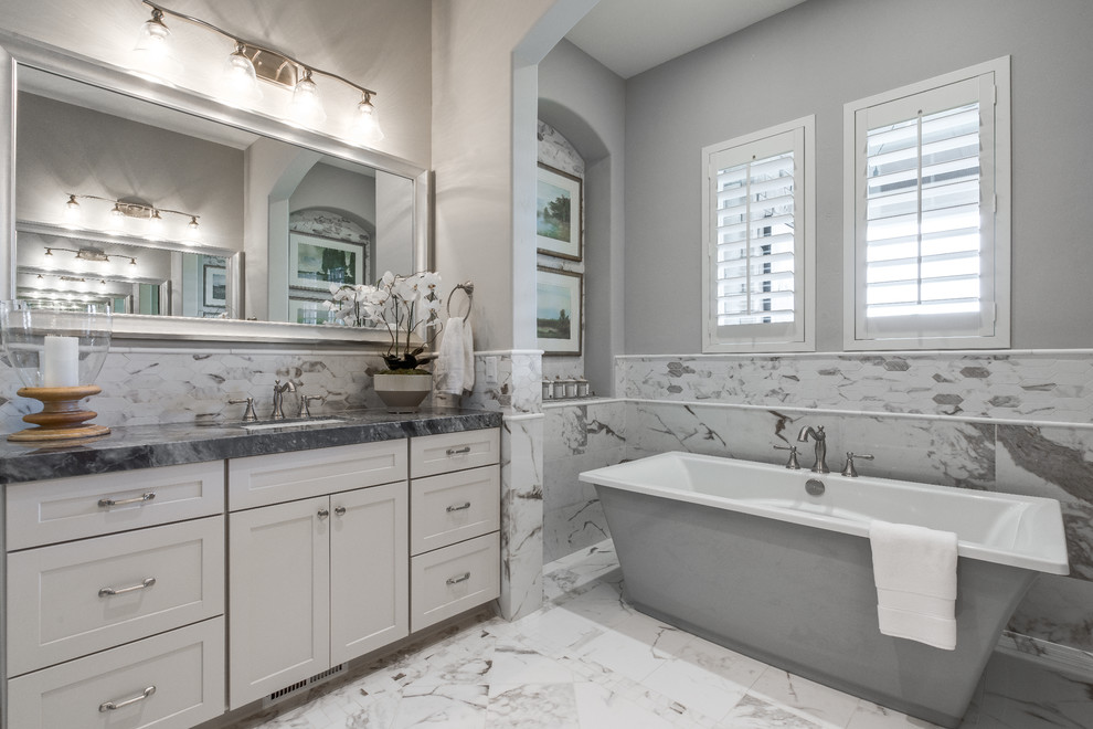 Inspiration for a large traditional ensuite bathroom in Salt Lake City with recessed-panel cabinets, white cabinets, a freestanding bath, a corner shower, a two-piece toilet, white tiles, ceramic tiles, grey walls, ceramic flooring, a submerged sink, granite worktops, a hinged door and white floors.