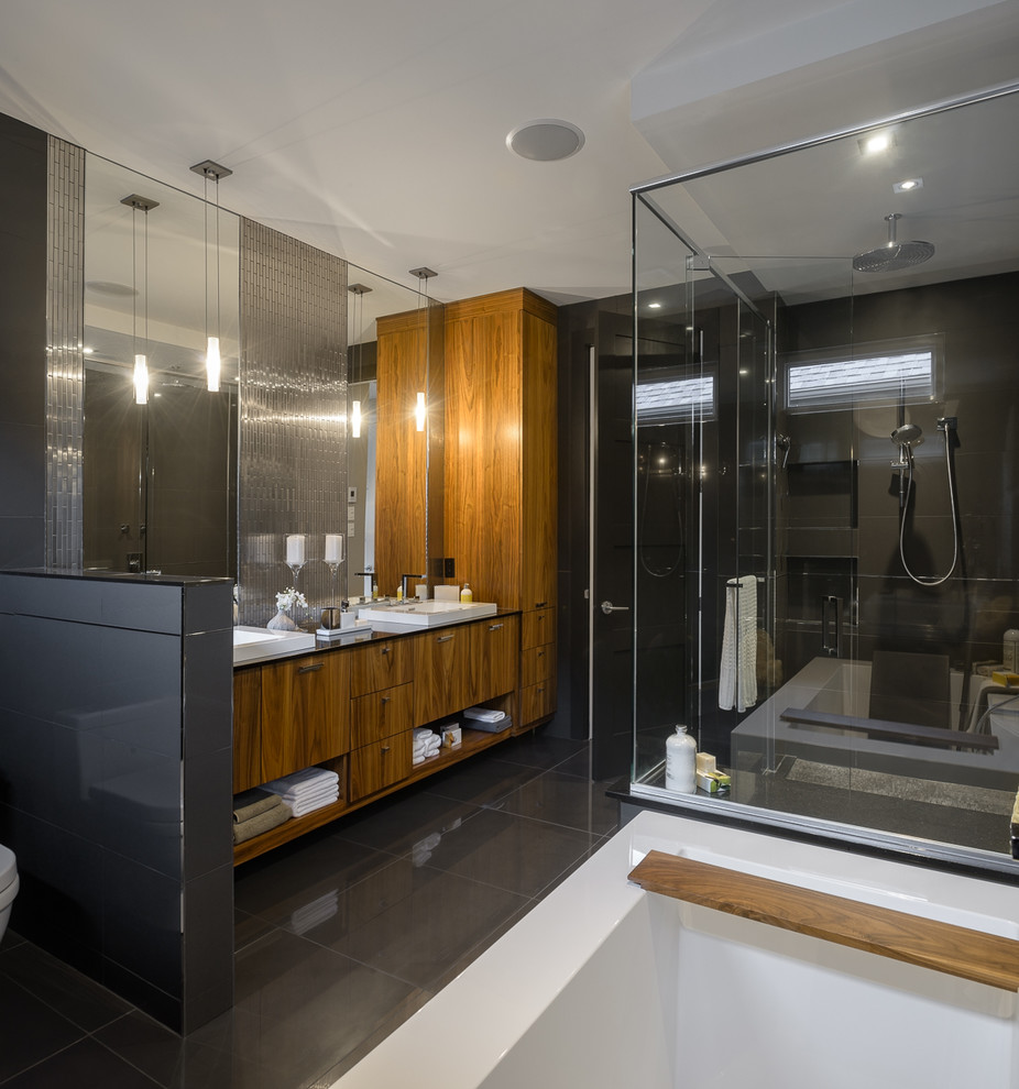 На фото: большая главная ванная комната в современном стиле с отдельно стоящей ванной, угловым душем, плоскими фасадами, фасадами цвета дерева среднего тона, унитазом-моноблоком, черной плиткой, керамогранитной плиткой и черными стенами