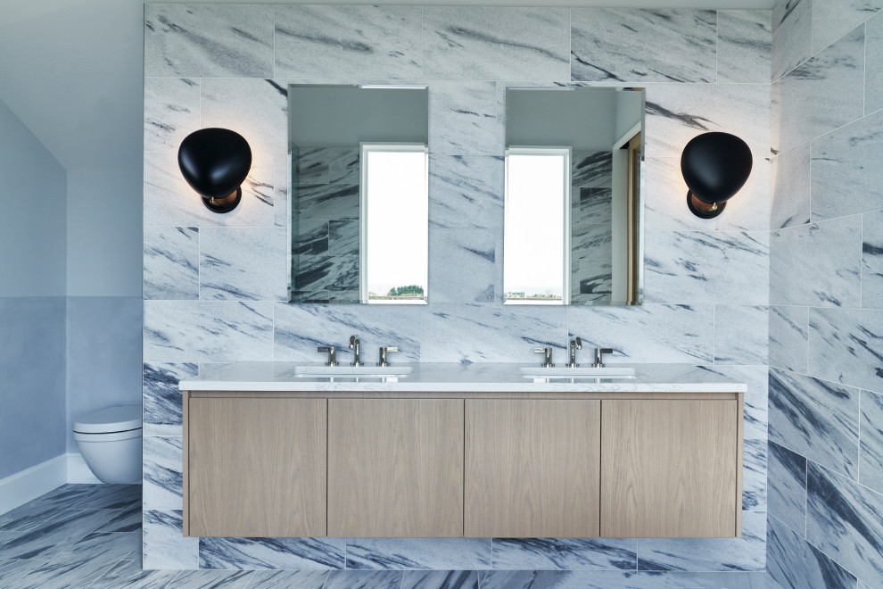 Modern inredning av ett en-suite badrum, med släta luckor, skåp i ljust trä, en vägghängd toalettstol, marmorkakel, marmorgolv, ett undermonterad handfat och marmorbänkskiva