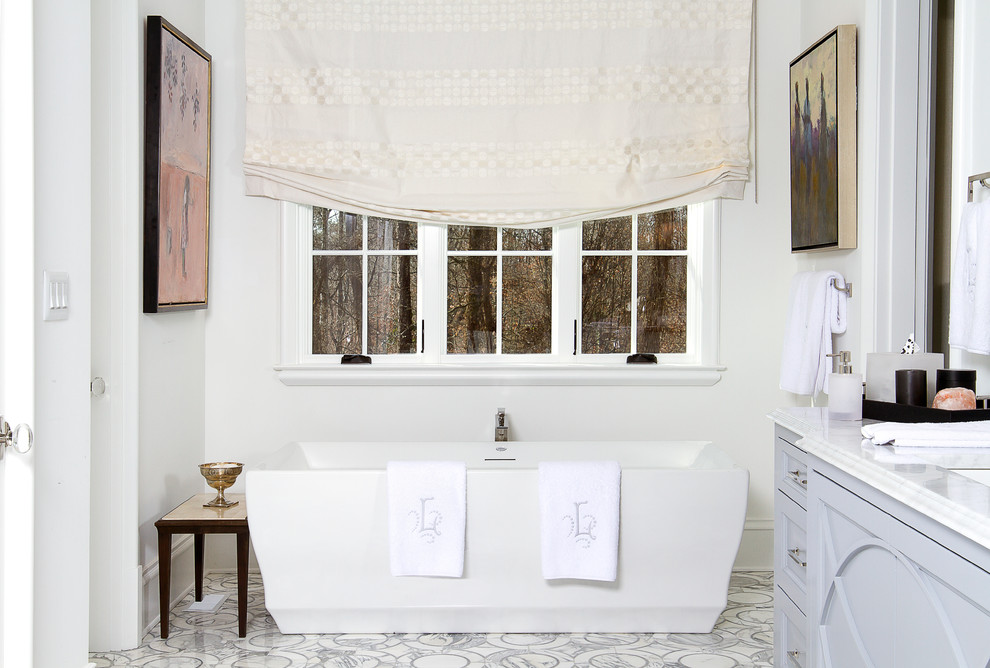 Стильный дизайн: огромная главная ванная комната в стиле неоклассика (современная классика) с фасадами островного типа, серыми фасадами, отдельно стоящей ванной, душем в нише, инсталляцией, белой плиткой, каменной плиткой, мраморным полом, мраморной столешницей, белыми стенами и врезной раковиной - последний тренд