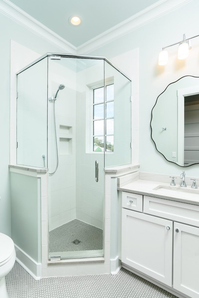 Cette photo montre une salle de bain bord de mer de taille moyenne avec un placard à porte shaker, des portes de placard blanches, WC à poser, un carrelage blanc, des carreaux de porcelaine, un mur bleu, un sol en carrelage de terre cuite, un lavabo encastré, un plan de toilette en marbre, un sol blanc et une cabine de douche à porte battante.