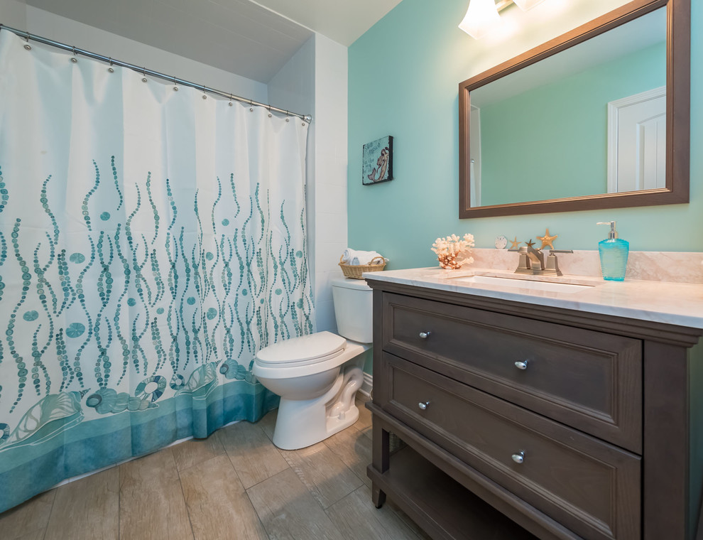 Tub/shower combo - small coastal 3/4 beige tile and porcelain tile porcelain tile tub/shower combo idea in Jacksonville with furniture-like cabinets, gray cabinets, a two-piece toilet, green walls, a drop-in sink and quartz countertops