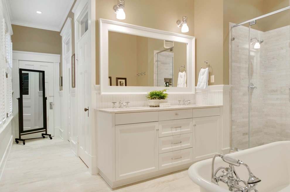 Идея дизайна: главная ванная комната среднего размера в классическом стиле с фасадами в стиле шейкер, белыми фасадами, ванной на ножках, душем в нише, унитазом-моноблоком, белой плиткой, мраморной плиткой, бежевыми стенами, полом из керамической плитки, врезной раковиной, столешницей из известняка, белым полом и душем с распашными дверями