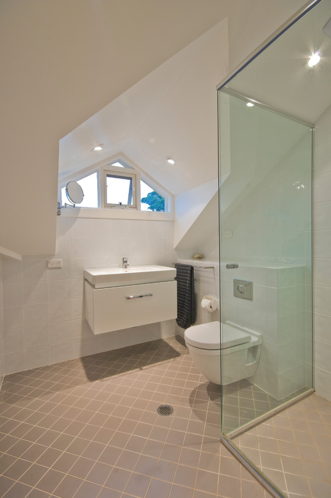 Modern inredning av ett badrum, med släta luckor, vita skåp, en vägghängd toalettstol, vit kakel, porslinskakel, klinkergolv i keramik och ett integrerad handfat