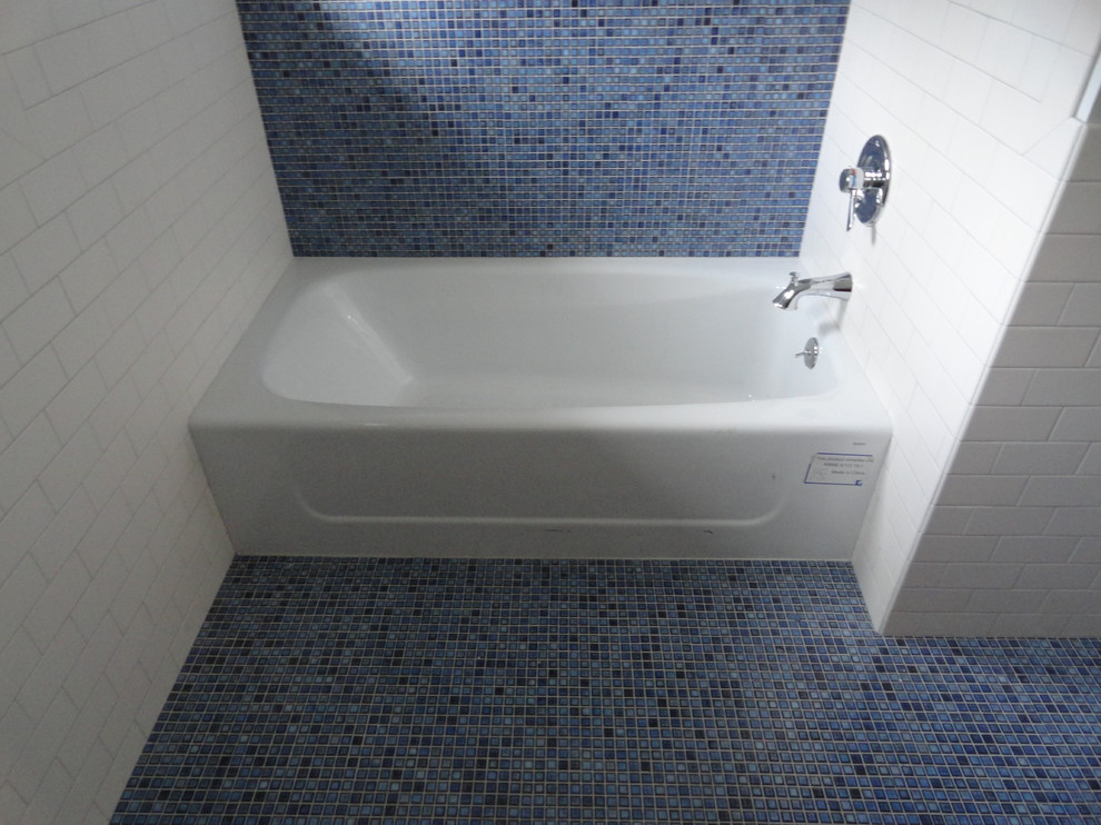 This is an example of a medium sized traditional shower room bathroom in New York with flat-panel cabinets, medium wood cabinets, an alcove bath, a shower/bath combination, a two-piece toilet, white tiles, metro tiles, blue walls, mosaic tile flooring, a submerged sink, solid surface worktops and blue floors.