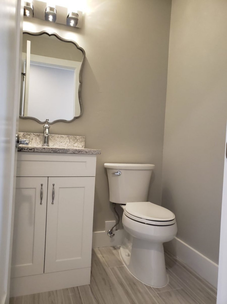 Klassisk inredning av ett mellanstort flerfärgad flerfärgat toalett, med luckor med infälld panel, vita skåp, en toalettstol med separat cisternkåpa, beige väggar, vinylgolv, ett undermonterad handfat, granitbänkskiva och grått golv