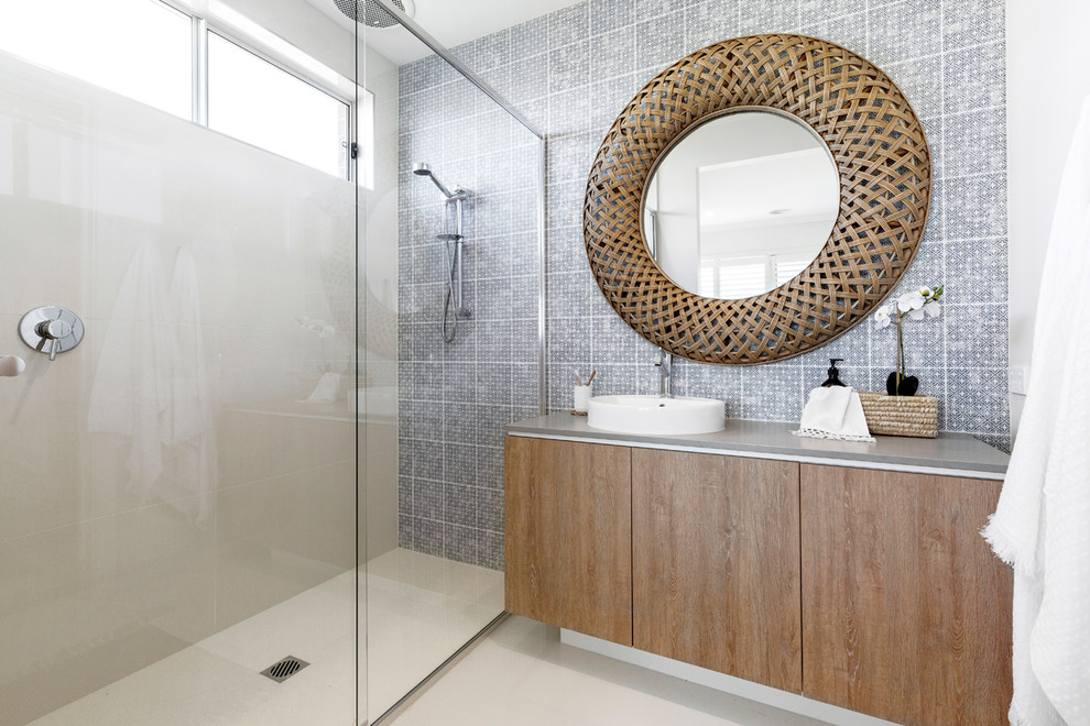 Beach style bathroom in Melbourne with flat-panel cabinets, medium wood cabinets, an alcove shower, blue tiles, white walls, a vessel sink, beige floors, a sliding door and grey worktops.
