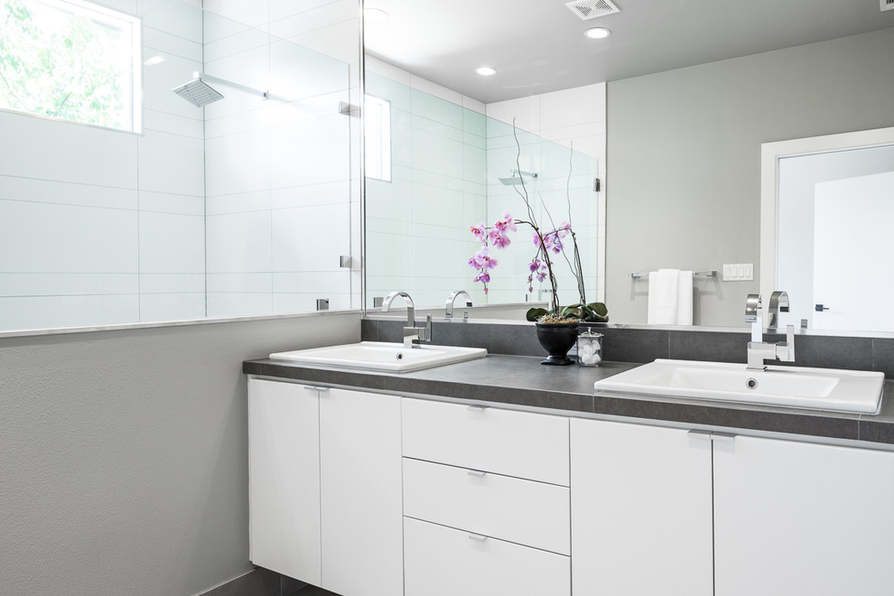 На фото: главная ванная комната в современном стиле с плоскими фасадами, белыми фасадами, двойным душем, серой плиткой, керамогранитной плиткой, серыми стенами, полом из керамогранита, накладной раковиной и столешницей из плитки