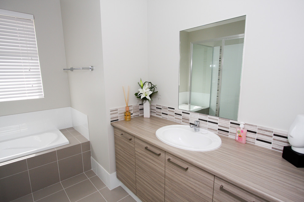 На фото: главная ванная комната среднего размера в современном стиле с накладной раковиной, плоскими фасадами, светлыми деревянными фасадами, столешницей из ламината, накладной ванной, бежевой плиткой и белыми стенами